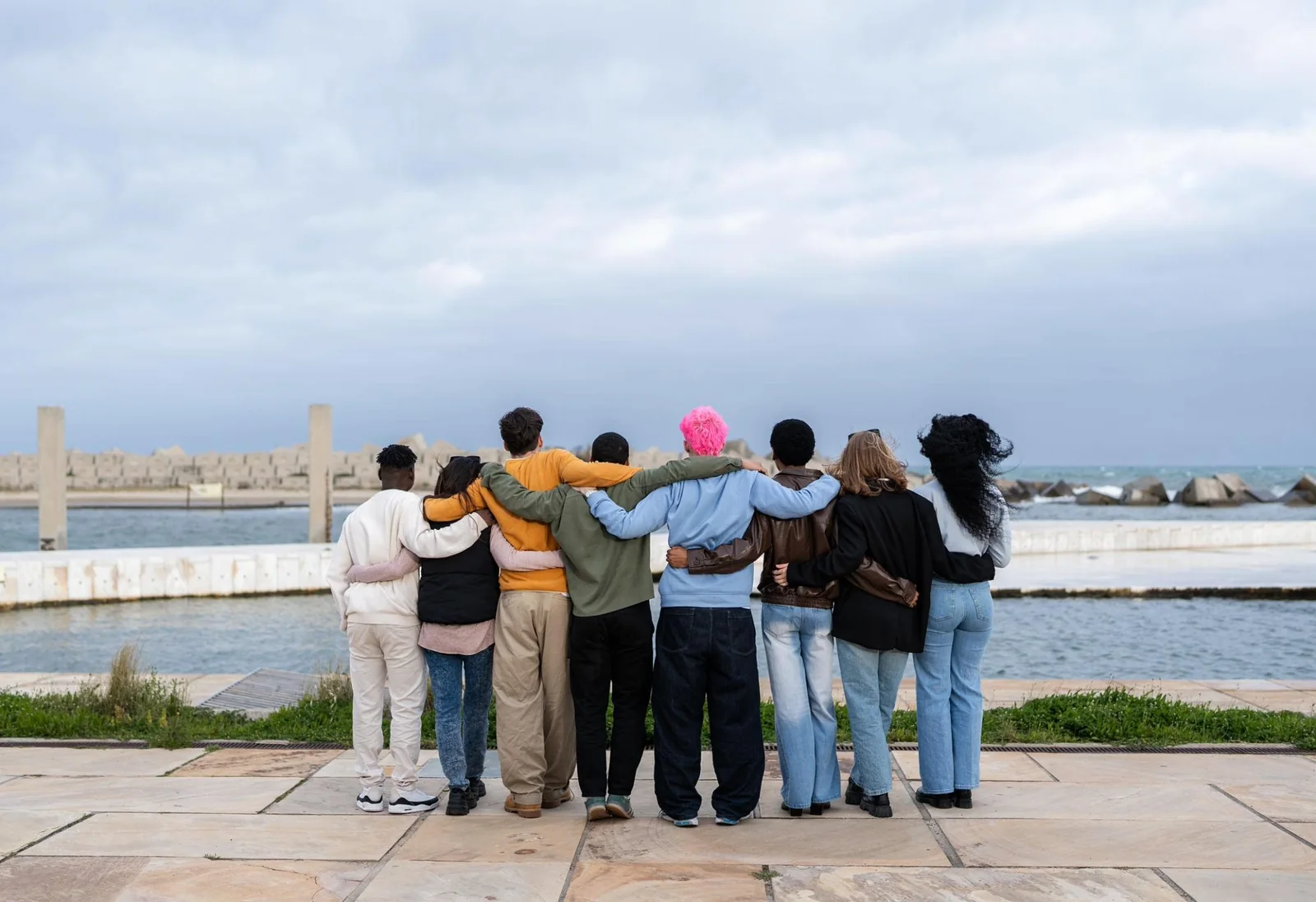 A group of young people standing arm in arm, looking out over the water