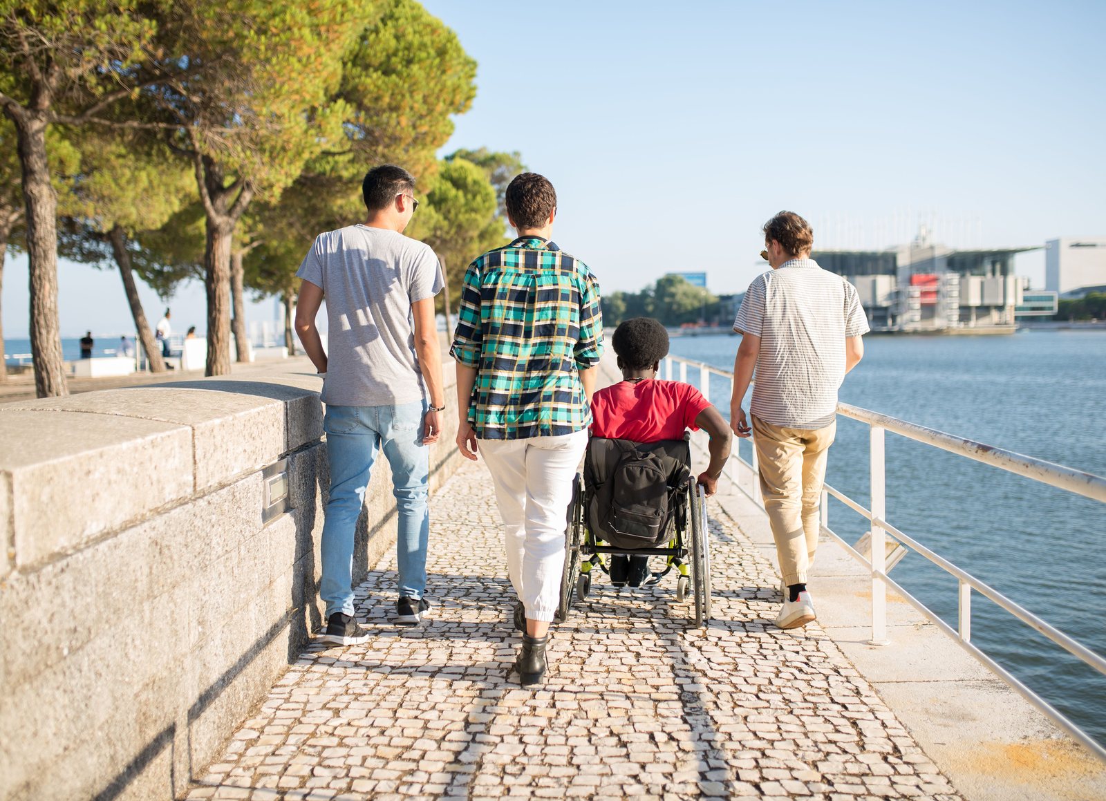 Four young people moving together along a waterfront, one of them a wheelchair user